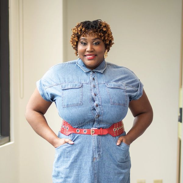 Confident woman in denim dress with red belt smiling.