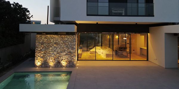 Modern house with illuminated stone wall and pool at dusk.