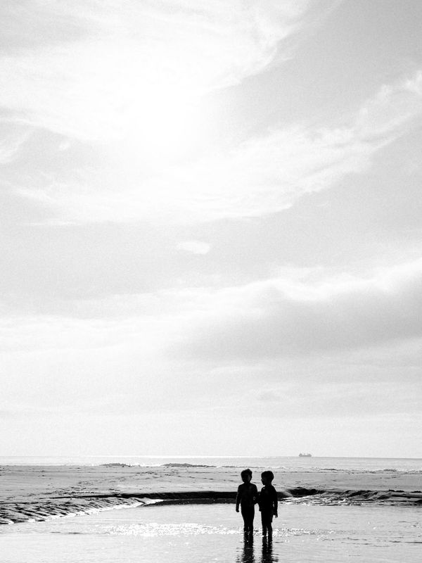 Two children stand together on a reflective beach under a bright sky.