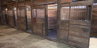 Empty wooden horse stalls inside a barn with hay on the floor.