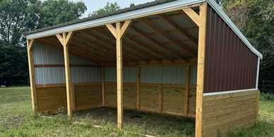 Open wooden shelter with metal roof in a grassy field.