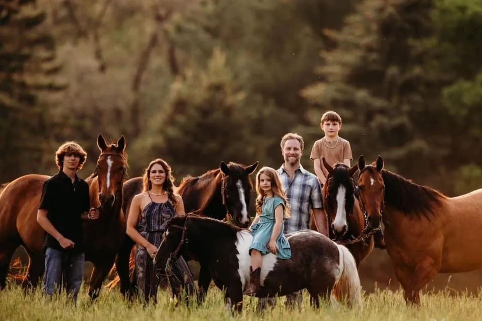 Family portrait with four people and five horses in a field during golden hour.