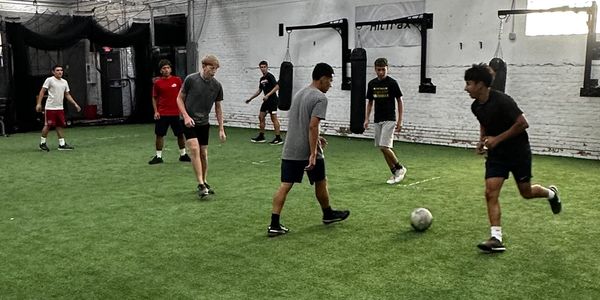 Young men playing soccer indoors on artificial turf.