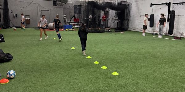 Indoor training facility with kids practicing soccer and boxing drills.