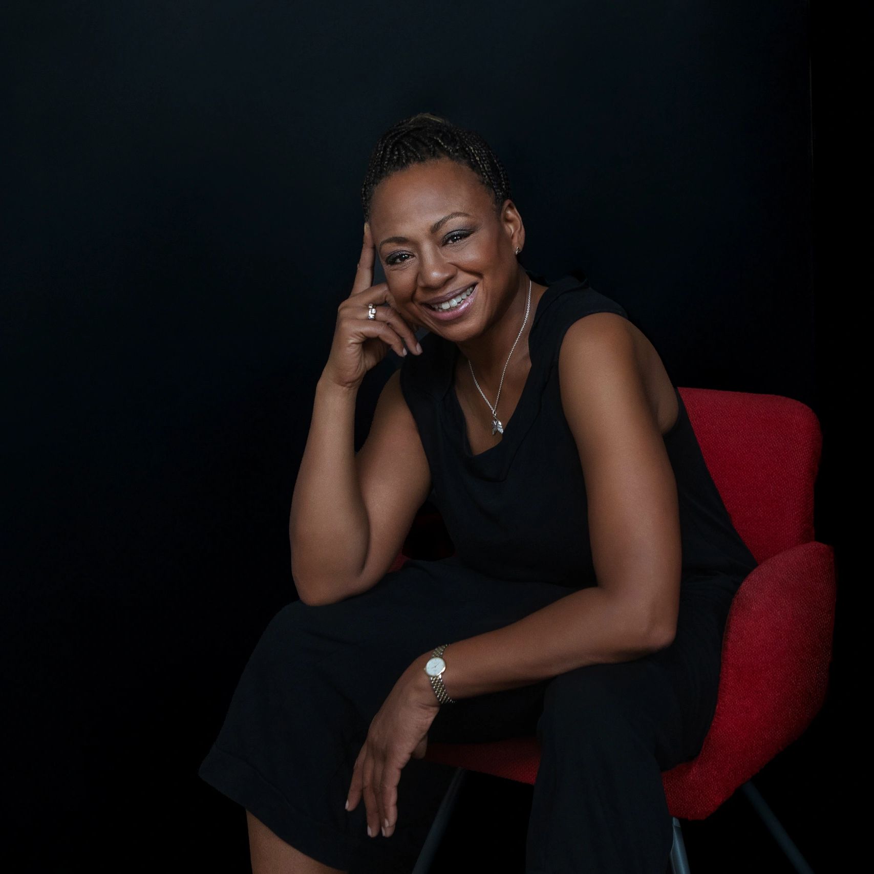 Smiling woman seated on a red chair against a dark background.