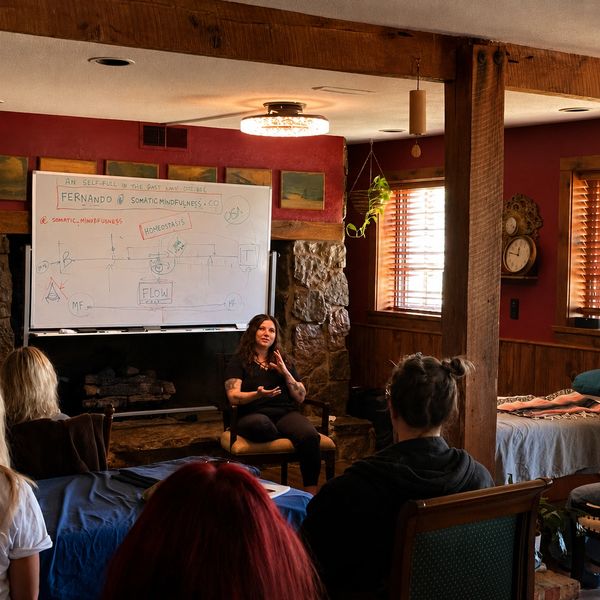 A woman teaches a mindfulness class in a cozy room with a whiteboard.