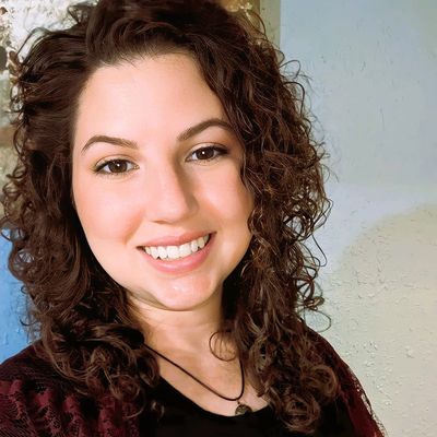 Young woman with curly hair smiling warmly at the camera.