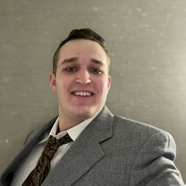 Smiling man in a gray suit and patterned tie.