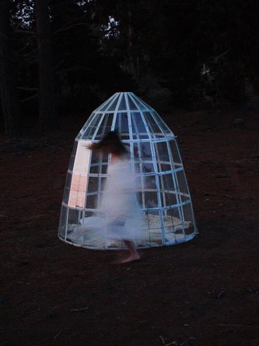 Blurred figure in white near a cage-like structure in a dark forest.