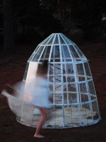 A blurred figure near a cage-like glass structure outdoors at dusk.