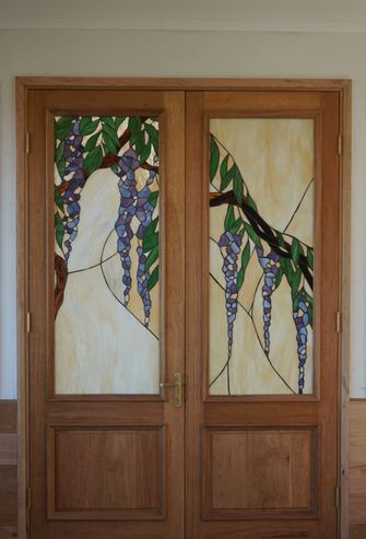 Wooden double doors with stained glass panels featuring purple wisteria and green leaves.