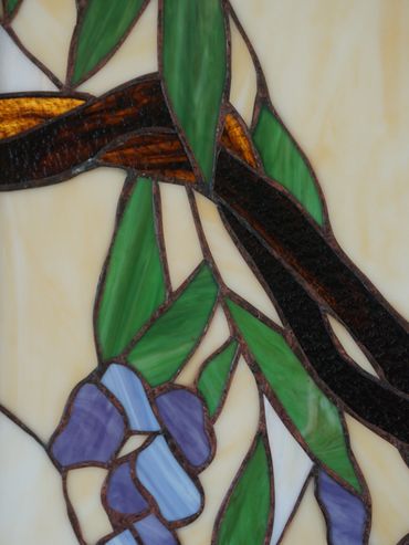 Close-up of a stained glass design featuring green leaves and purple flowers.