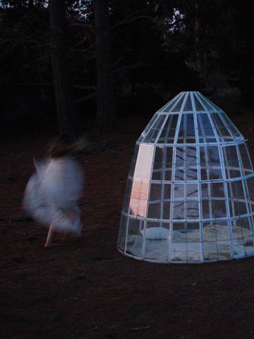A blurred figure dances near a glowing geometric cage at night.