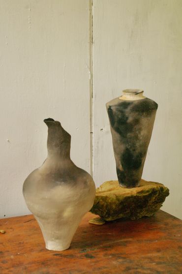 Two uniquely shaped ceramic vases with a smoky finish on a wooden surface.