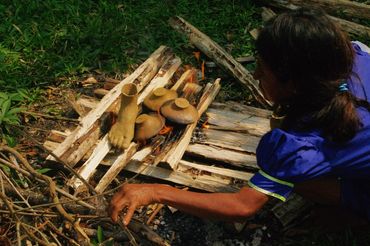 Person preparing traditional clay pots on a wooden fire setup outdoors.