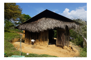 A rustic hut with a thatched roof in a rural setting under a clear sky.