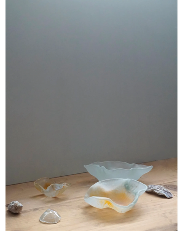 Delicate glass art pieces arranged on a wooden surface against a plain wall.
