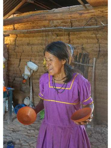 Woman in traditional dress holding two clay bowls inside a rustic room.