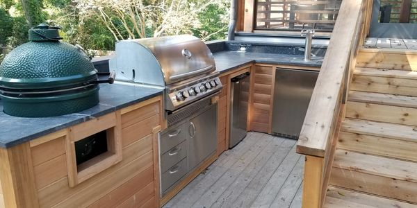 Outdoor kitchen with stainless steel grill and wooden deck stairs.