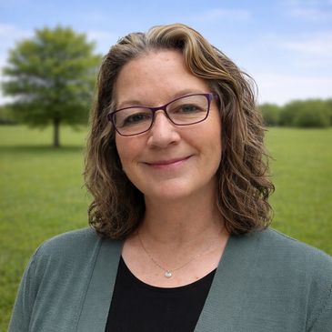 Smiling woman with glasses standing outdoors on a sunny day.