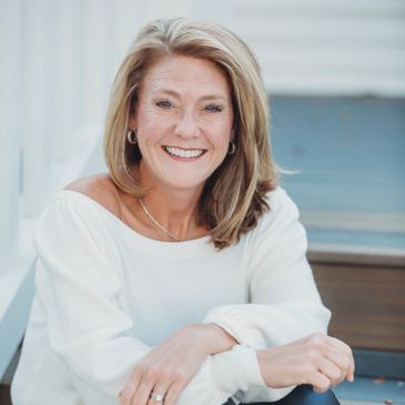 Smiling woman in white top sitting outdoors.