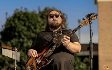 Musician playing bass guitar outdoors.