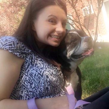 A woman smiling with her dog outdoors on a sunny day.