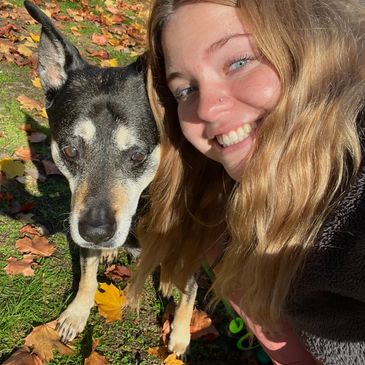 Smiling young woman taking a selfie with her black and white dog outdoors.
