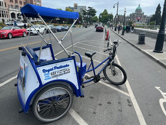 A blue Royal Pedicab parked on a city street near a historic building with a Canadian flag.