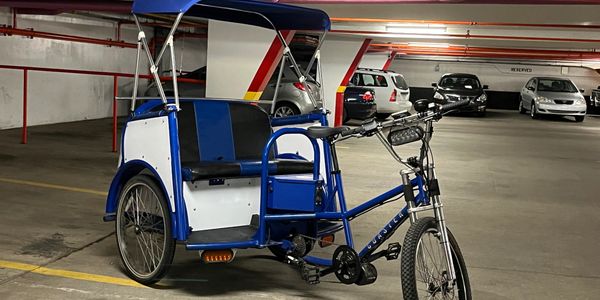 A blue pedicab parked in an underground parking garage.