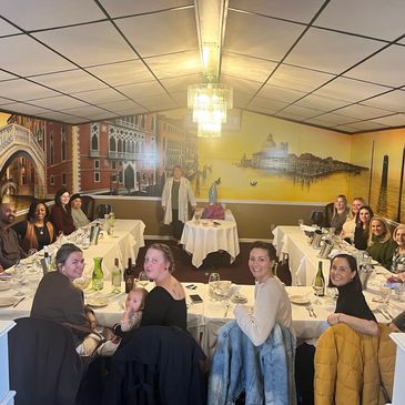 Group of people seated around tables in a cozy restaurant with a mural backdrop.