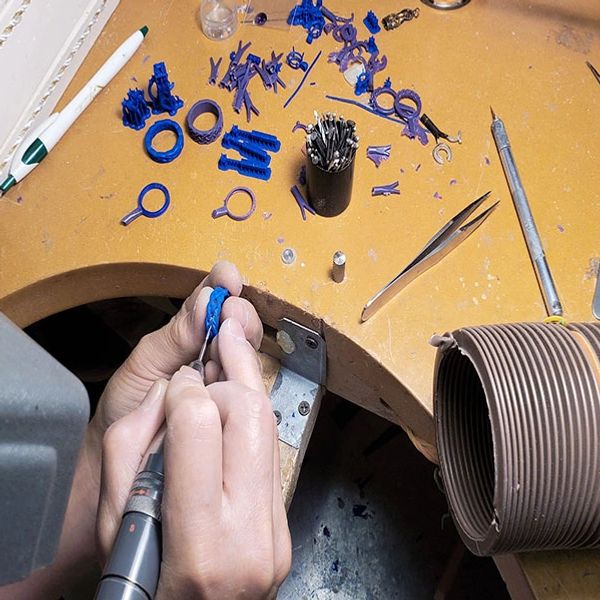 Jeweler hand carving a wax mold ring with a bur at the workbench. 