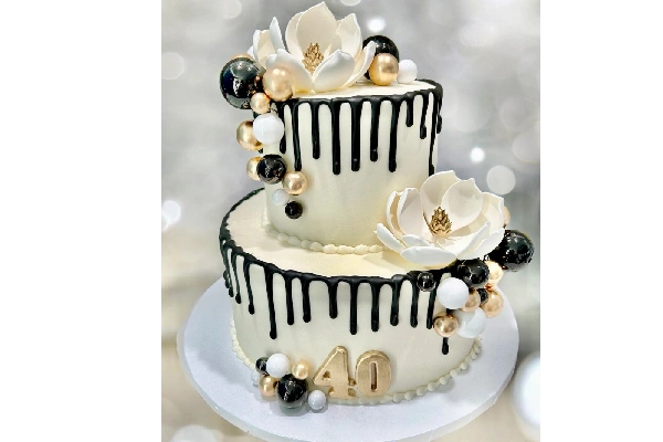 Elegant two-tier white cake with black drip, gold accents, flowers, and '40' topper.