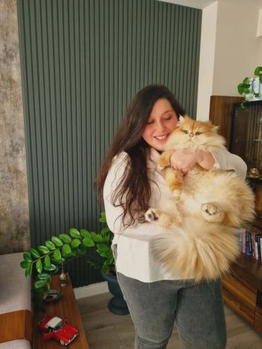 Woman smiling while holding a fluffy orange cat.