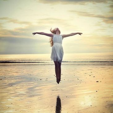 Girl in white dress joyfully jumping on the beach.