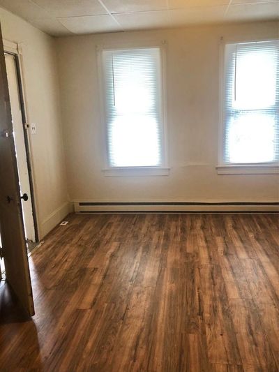 Empty room with wooden flooring and two windows with blinds.