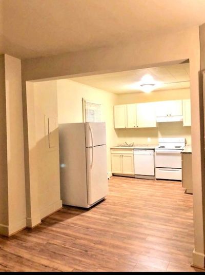 Empty kitchen with white appliances and wood floor.