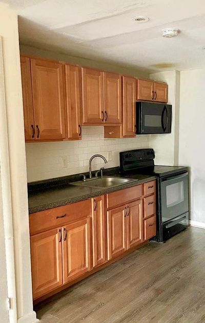Compact kitchen with wooden cabinets, black appliances, and a single sink.