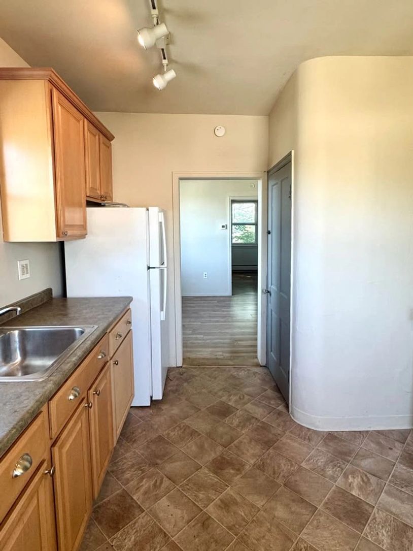 Small kitchen with wooden cabinets and beige tiled floor.