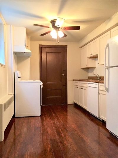 Narrow kitchen with white appliances, wooden floor, and a ceiling fan light.