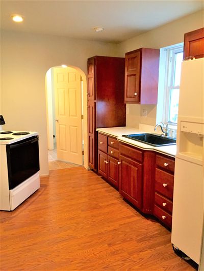 Bright kitchen with wooden floors and cabinets, white appliances, and an arched doorway.