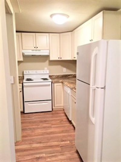 Compact kitchen with white appliances and wooden flooring.