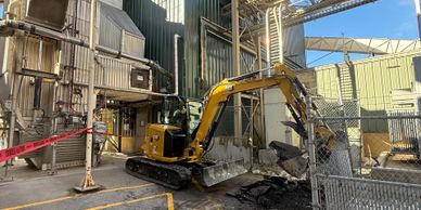Yellow excavator working inside industrial facility with metal structures.