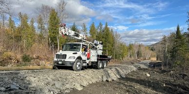 Utility truck with bucket lift on a rocky rural road under a blue sky.