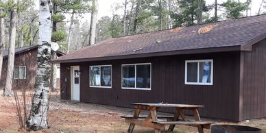 Rustic brown cabin surrounded by trees with a picnic table outside.