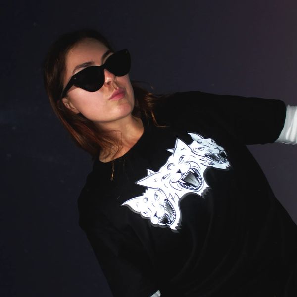Woman wearing sunglasses and a black shirt with a three-headed wolf design.