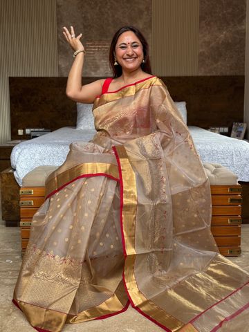A smiling woman in a traditional golden saree sitting on a bed.
