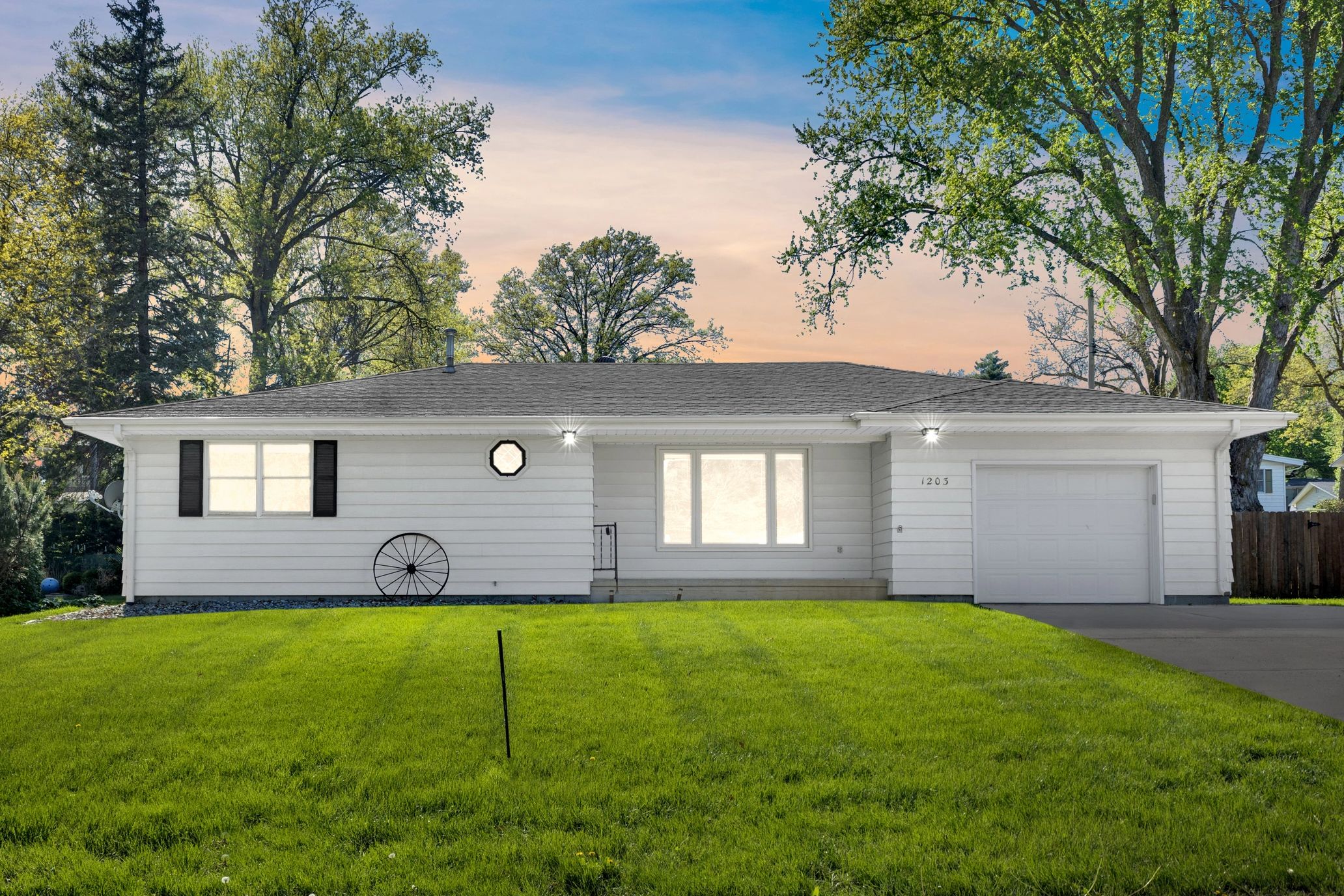 White single-story house with green lawn and trees at sunset.