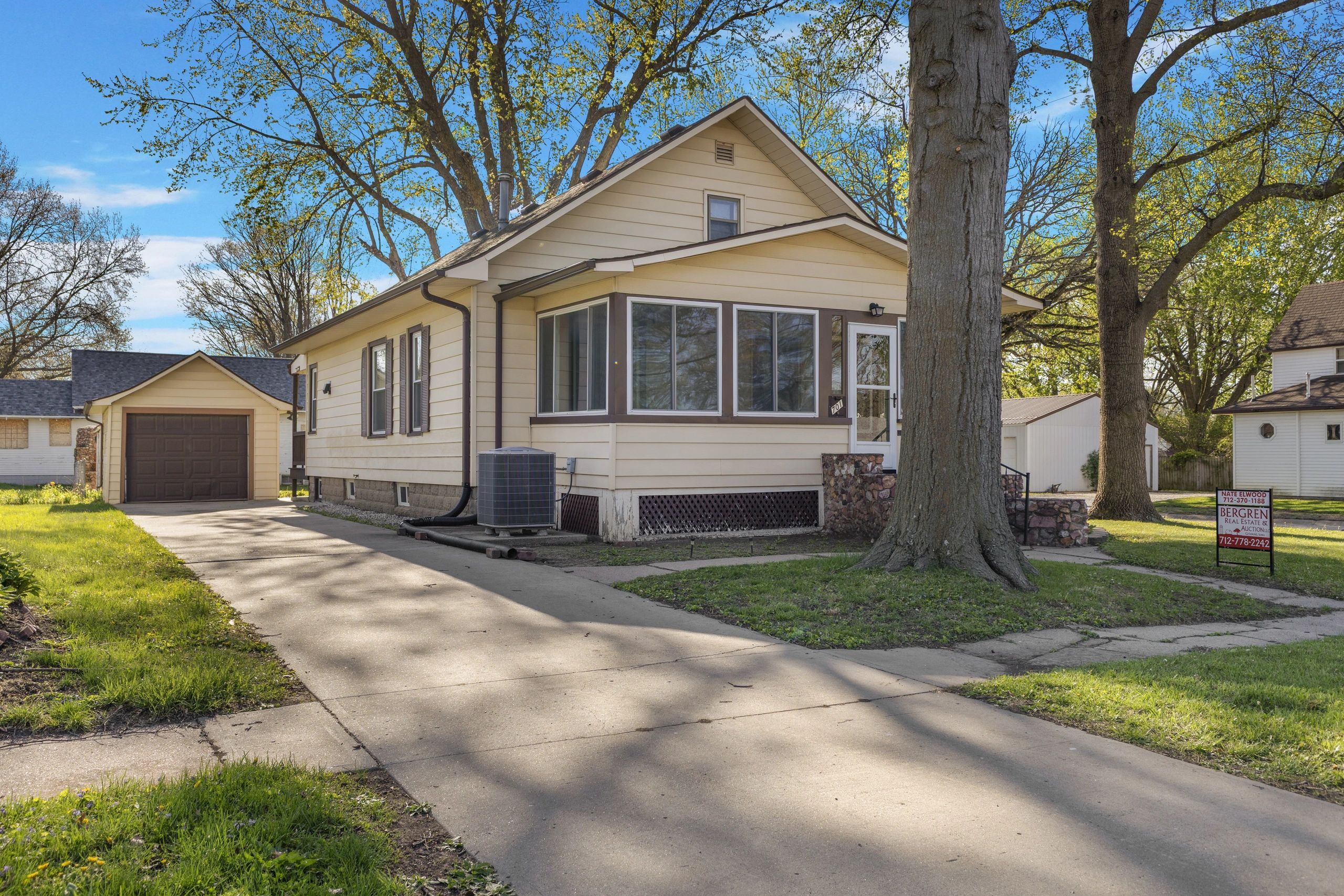 Cozy beige house with attached garage and large trees in front yard.