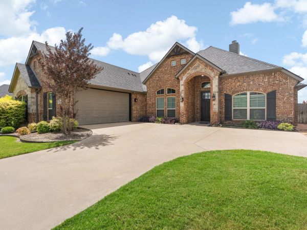 Brick house with a large driveway and green lawn.